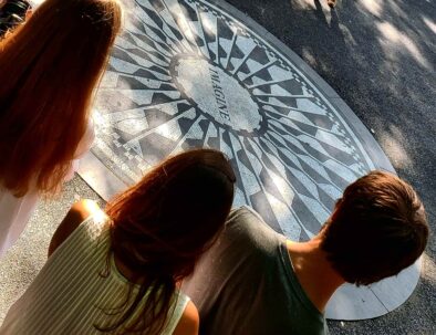 Mosaico de Imagine en Central Park, NYC, con tres figuras de adolescentes de espaldas en primer plano.