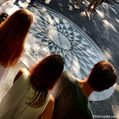 Mosaico de Imagine en Central Park, NYC, con tres figuras de adolescentes de espaldas en primer plano.
